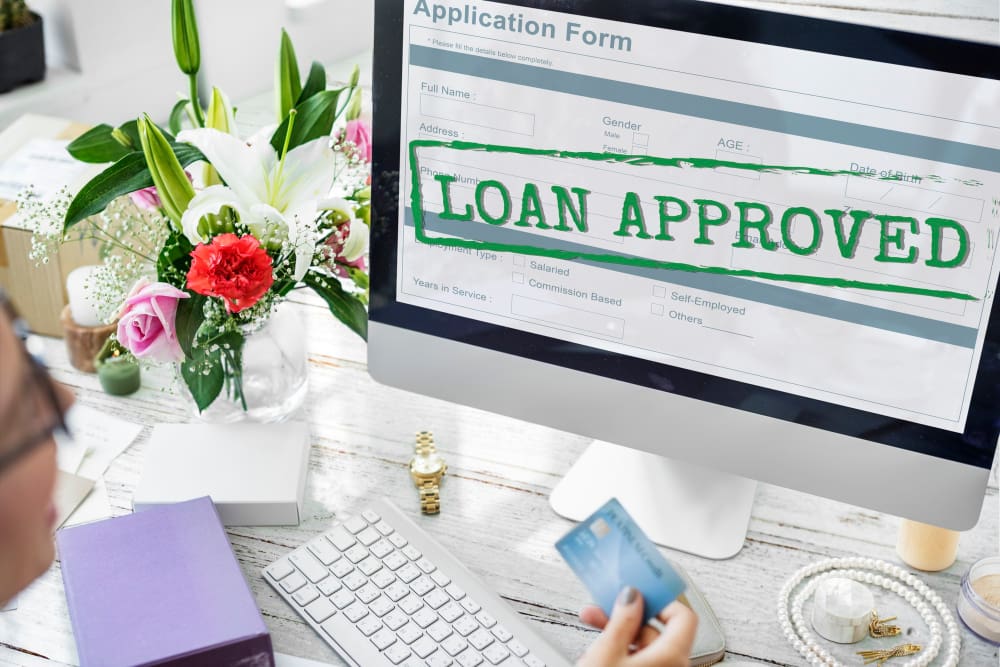 Computer screen showing 'Loan Approved' with a person holding a credit card.
